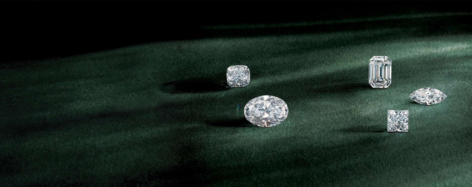 pear emerald princess cushion and marquise cut loose diamonds sitting on a soft green surface 