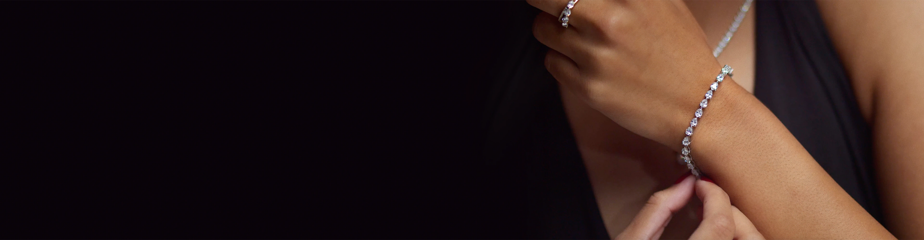 woman holding her arm across her body touching a pear shaped diamond line tennis bracelet secured on her wrist