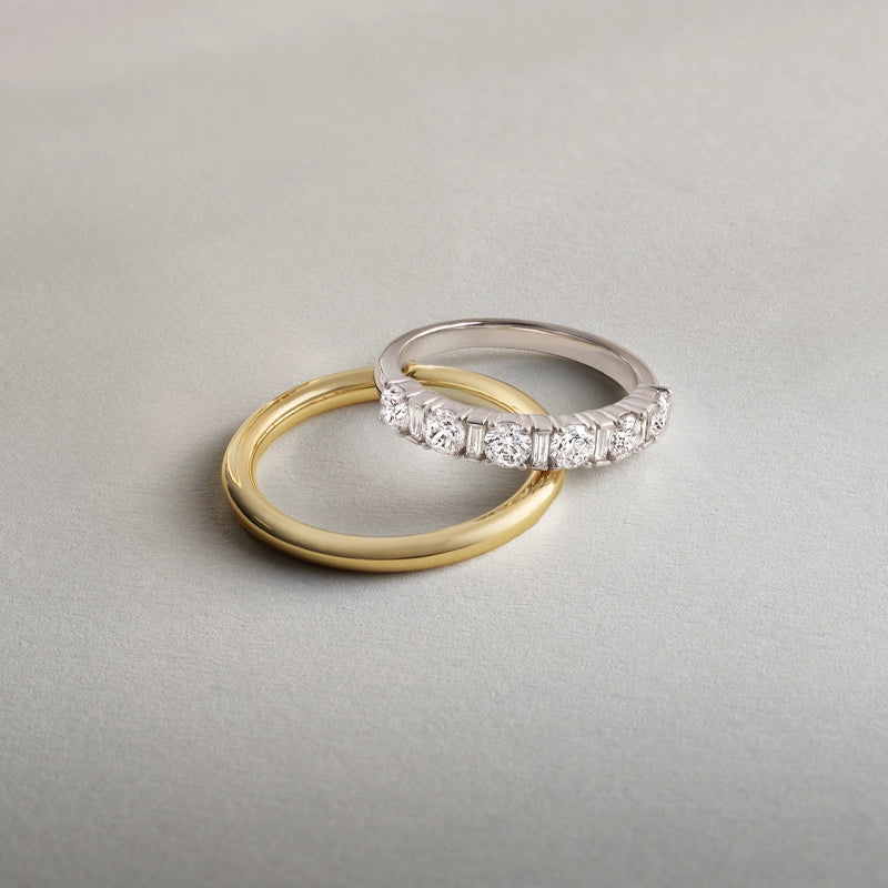 plain yellow gold band and a white gold diamond wedding band laying on a grey surface